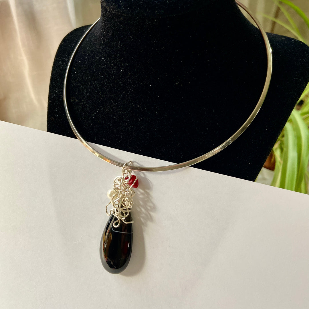 Black teardrop Agate pendant, silver-plated wire wrap and red gemstone  against a white background