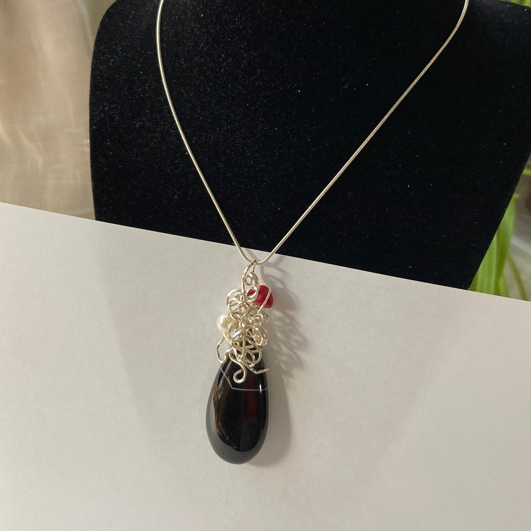 Necklace Black teardrop Agate pendant, silver-plated wire wrap and red gemstone on a white surface