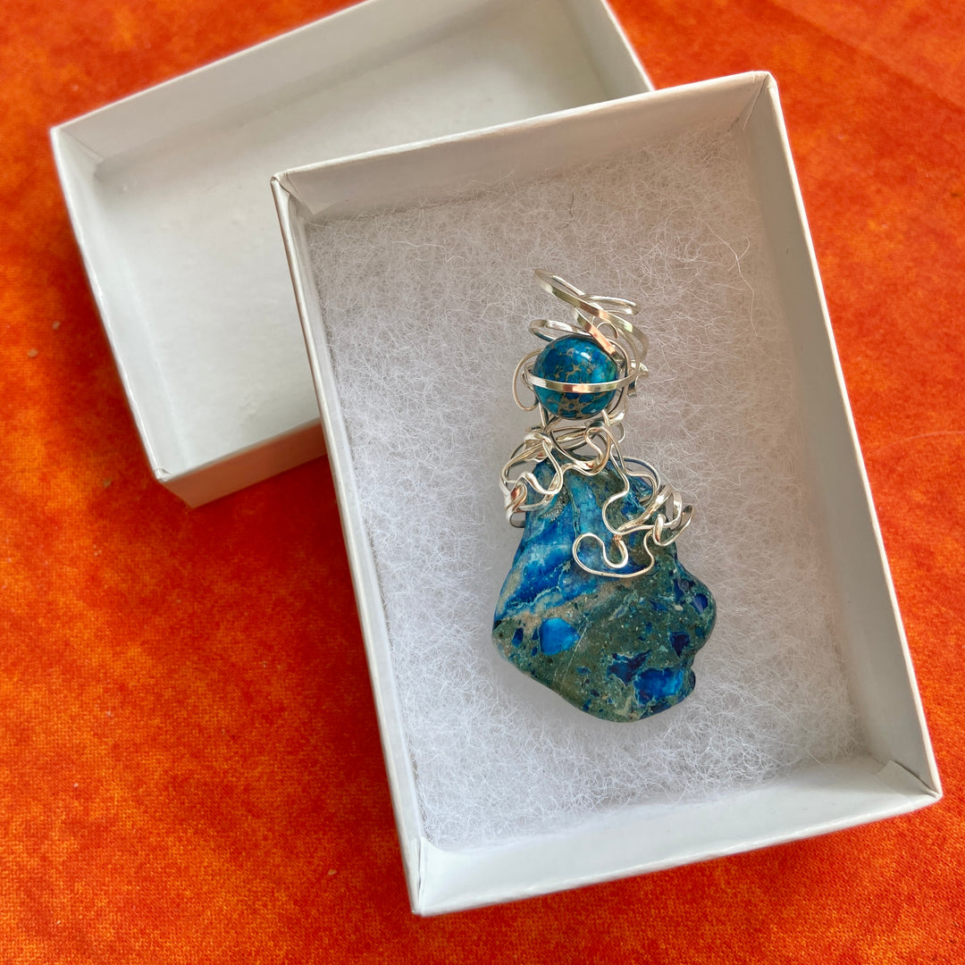 Blue Jasper stone pendant with silver-plated wire in a white box on an orange surface