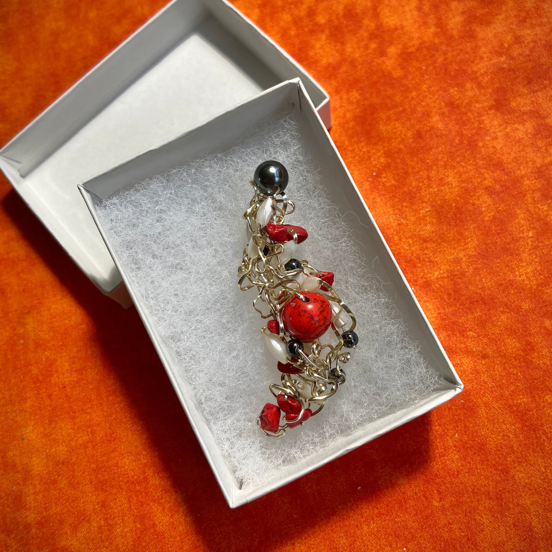 Pendant with red Jasper stones and black beads in a white box on an orange surface