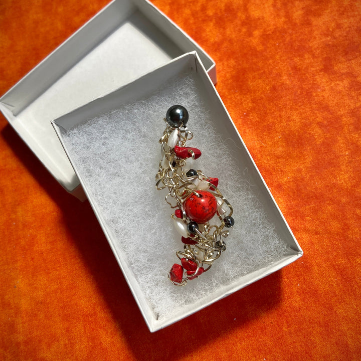 Pendant with red Jasper stones and black beads in a white box on an orange surface