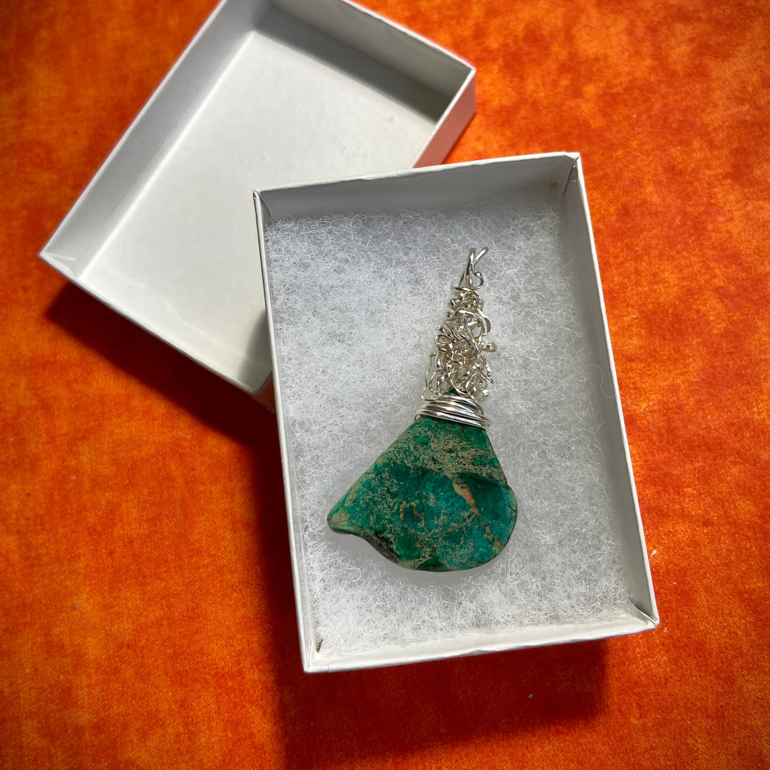 Jewelry box with a green Jasper gemstone and silver wire wrap pendant on an orange surface