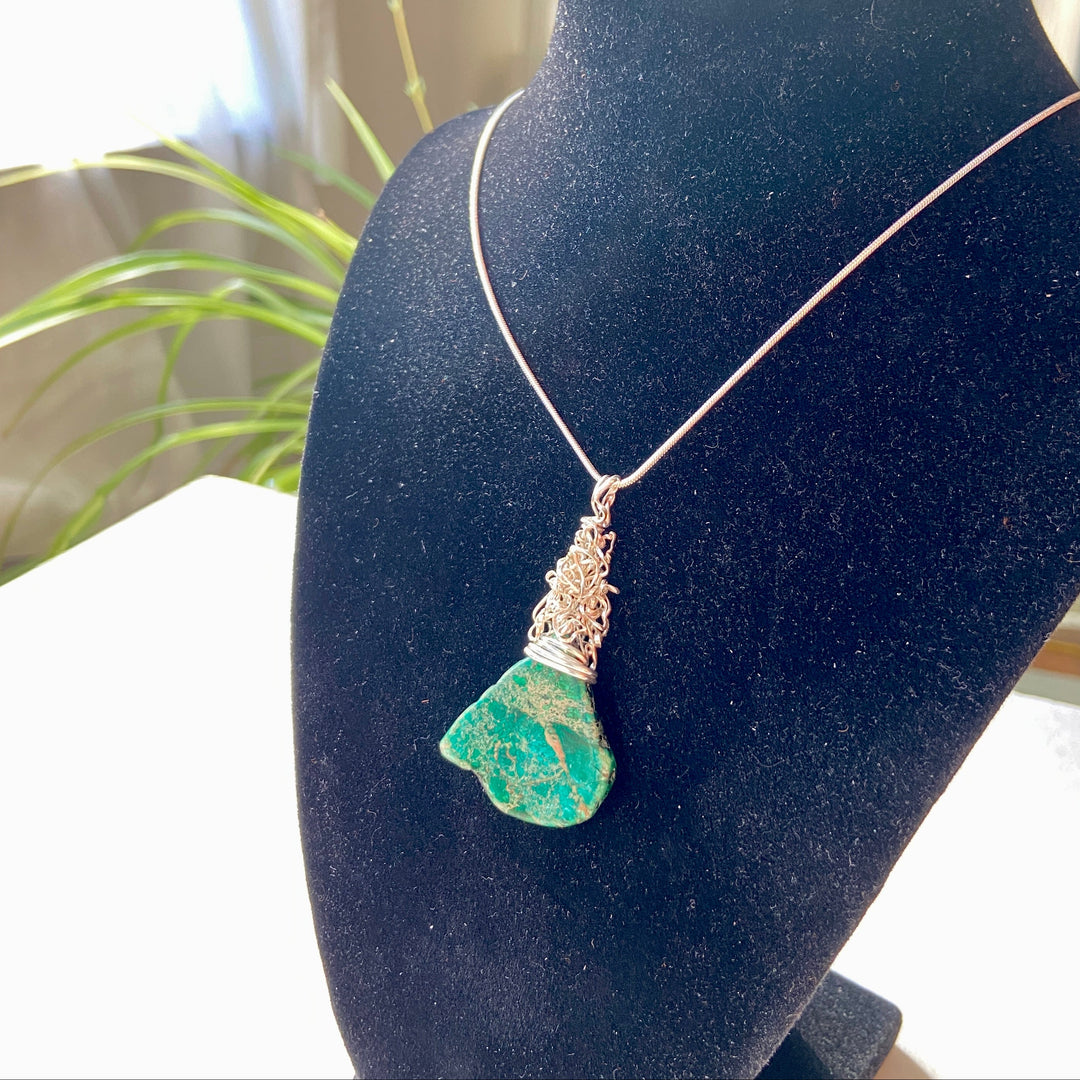 green Jasper gemstone and silver wire wrap pendant on a black diaplay