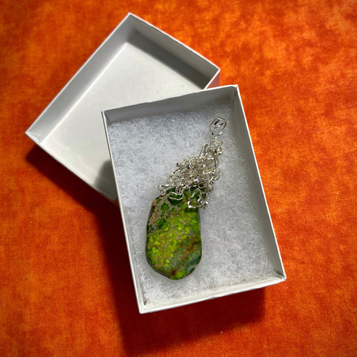 Jewelry box with a green Jasper stone pendant and silver-plated wire wrap on an orange background