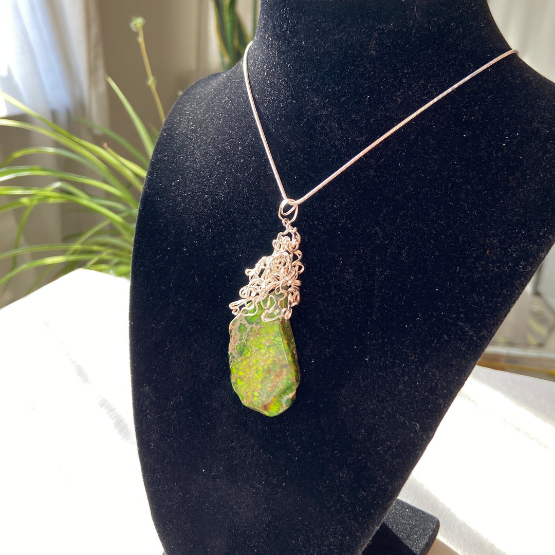 Necklace with a green Jasper stone pendant and silver-plated wire wrap on a black velvet stand