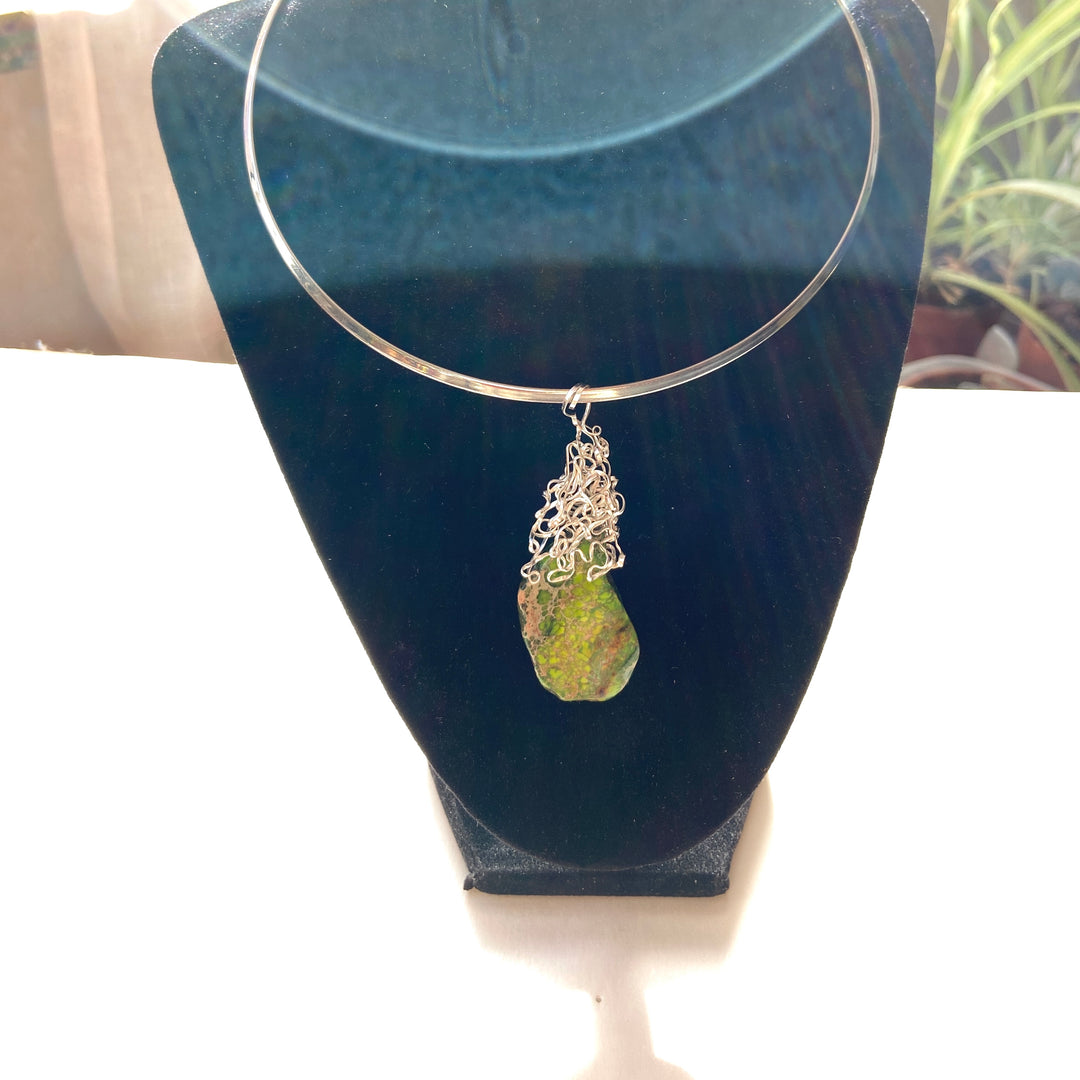 Necklace with green Jasper stone pendant and silver-plated wire wrap on a black display stand.