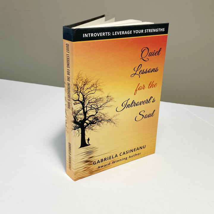 A hardcover book titled 'Quiet Lessons for the Introvert’s Soul' by Gabriela Casineanu, displayed on a flat surface with a tree silhouette against a sunset on the cover.
