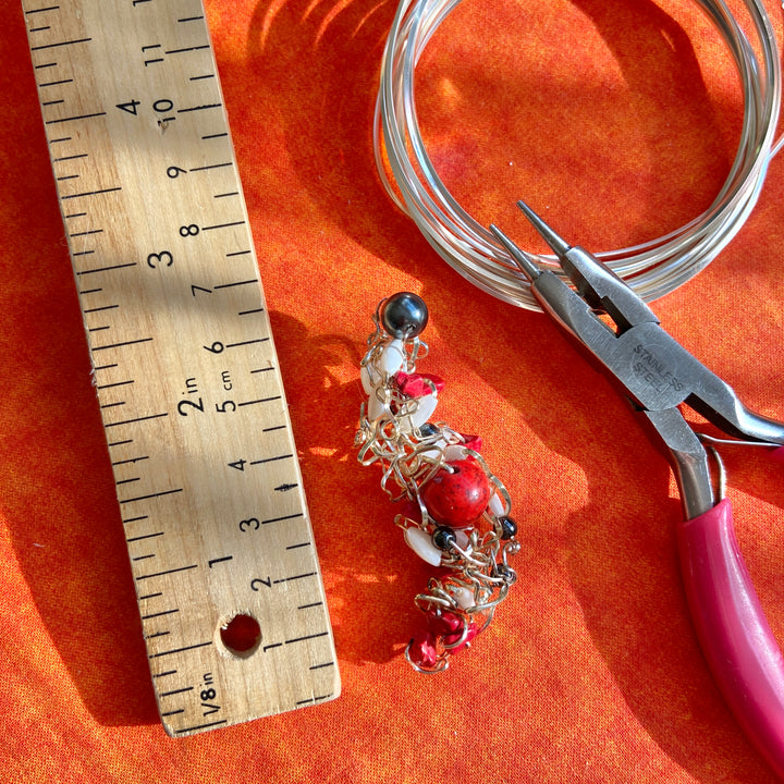 Jewelry-making setup with a beaded necklace, pliers, and ruler on an orange surface