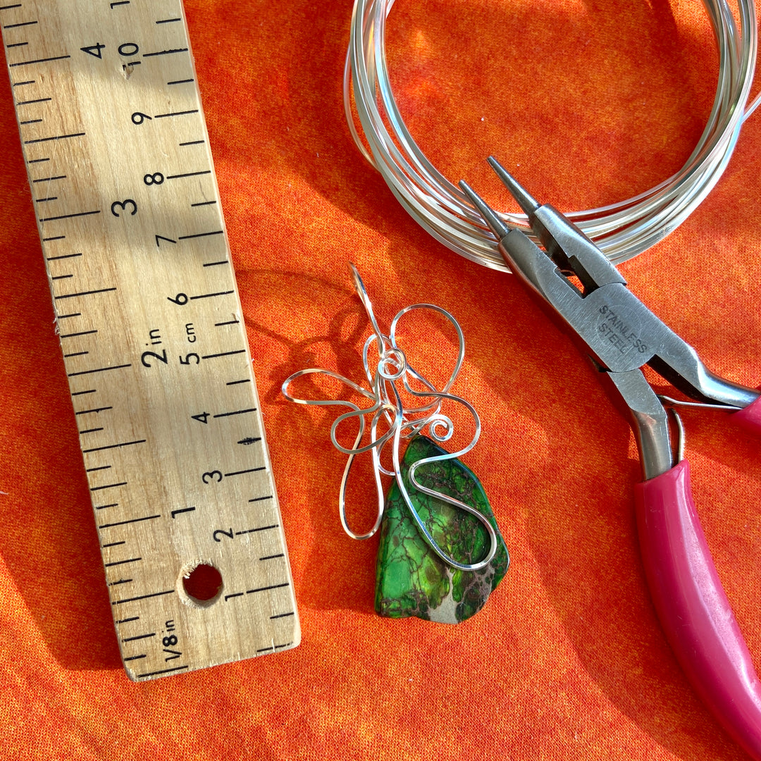 Jewelry-making tools including wire, pliers, and a ruler on an orange surface