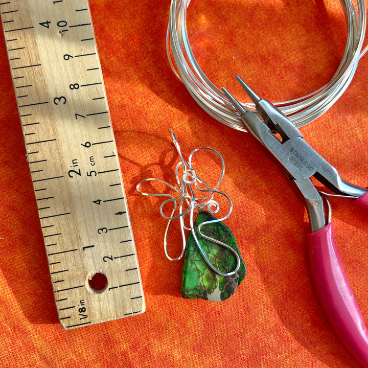 Jewelry-making tools including wire, pliers, and a ruler on an orange surface