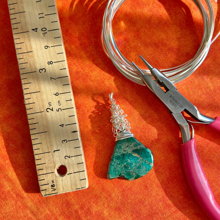Jewelry-making tools including wire, pliers, and a turquoise stone on an orange surface with a ruler.