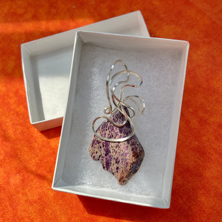 Silver pendant with a purple stone in a white box on an orange background