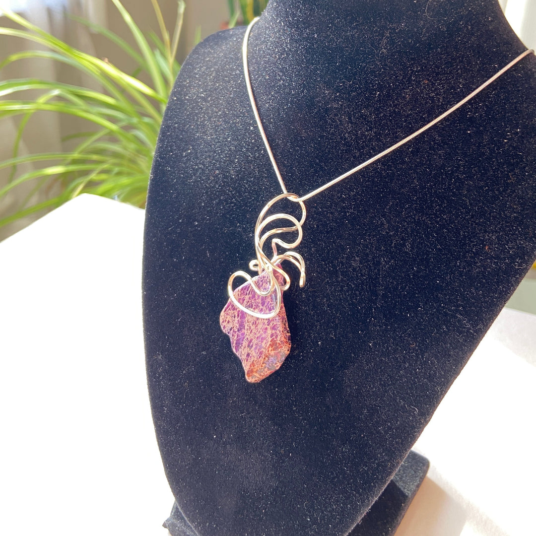 wire-wrapped purple Jasper stone pendant on a black display